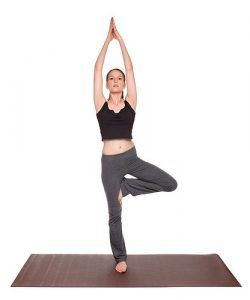 Isolated studio shot of a fit Caucasian woman holding the vrksasana Tree Pose yoga position on an exercise mat.